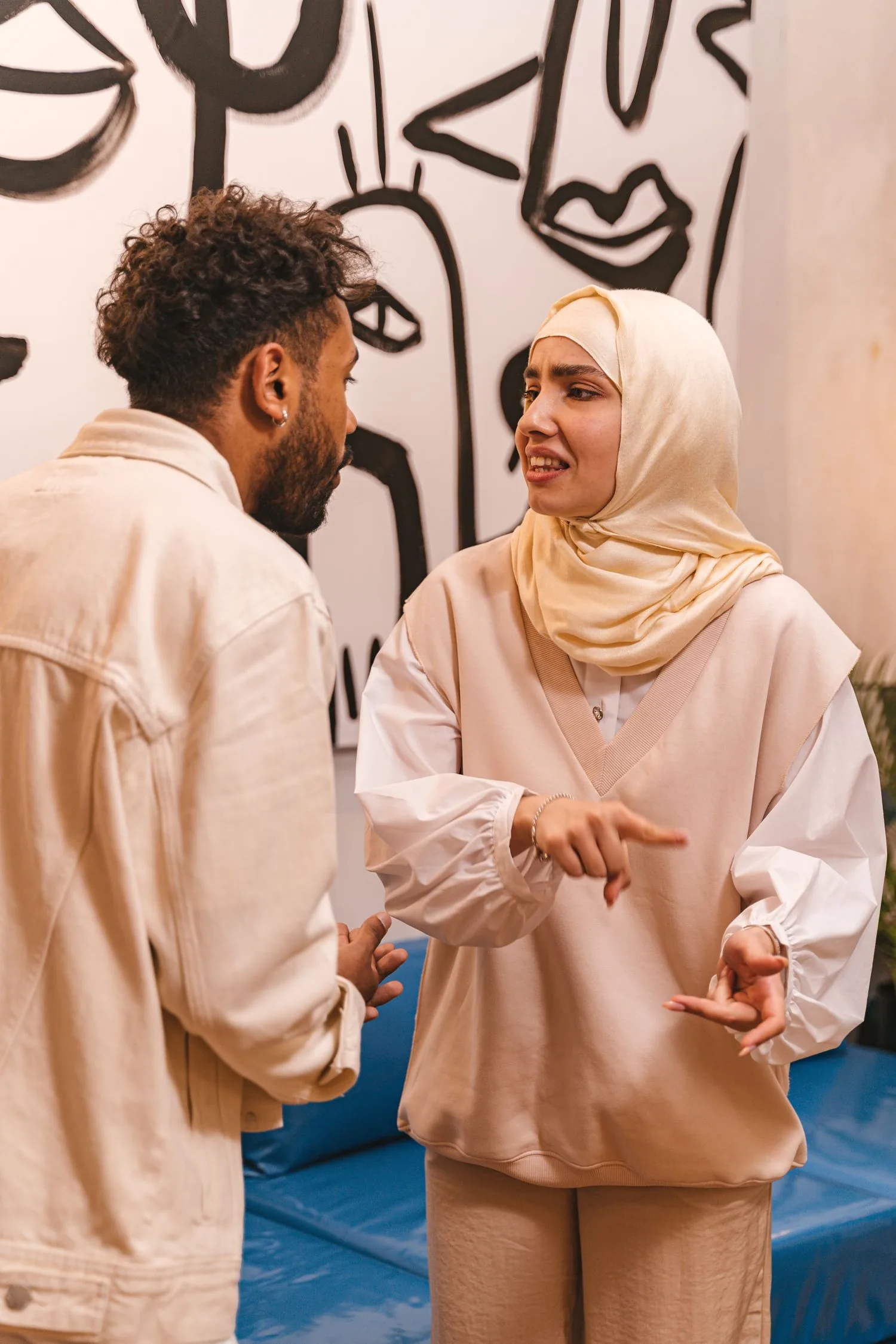 Une femme en hijab, debout, parle avec les mains à son mari qui lui fait face et l’écoute.
